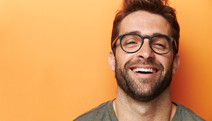 Man with glasses smiling against orange background